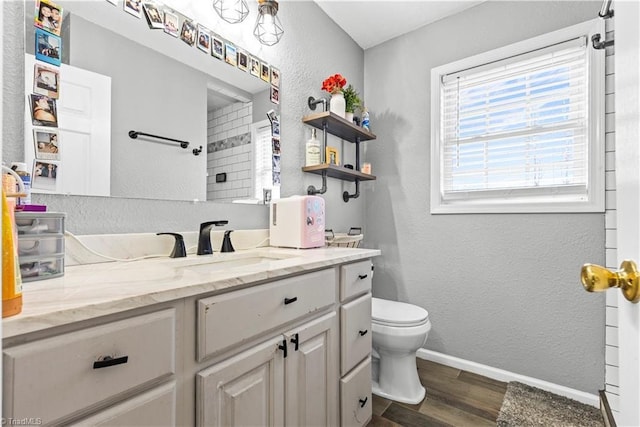 bathroom with a textured wall, toilet, vanity, wood finished floors, and baseboards