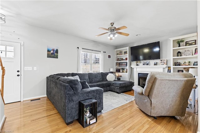 living room with ceiling fan, light wood finished floors, a fireplace, and visible vents