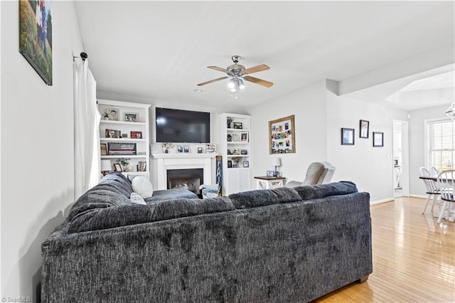 living room with light wood-style floors, a fireplace, baseboards, and ceiling fan