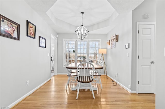 dining room featuring a chandelier, light wood-type flooring, a raised ceiling, and baseboards