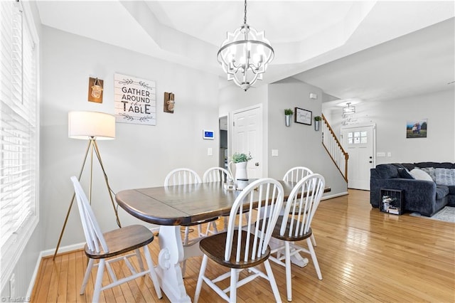 dining space featuring a tray ceiling, light wood finished floors, an inviting chandelier, baseboards, and stairs