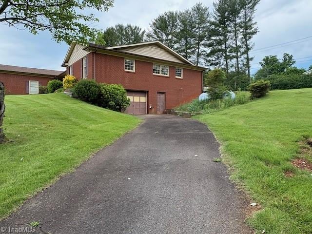 view of side of home with an attached garage, driveway, a lawn, and brick siding
