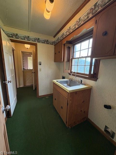 kitchen with a sink, a textured ceiling, light countertops, wallpapered walls, and dark colored carpet