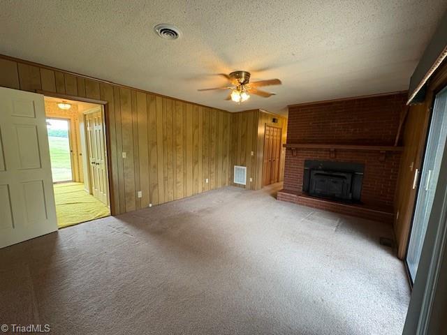 unfurnished living room with a ceiling fan, a textured ceiling, carpet, a brick fireplace, and wooden walls