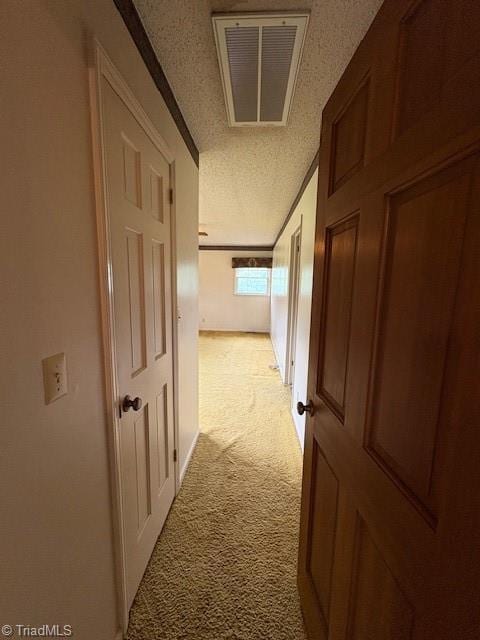 hall featuring a textured ceiling, light colored carpet, and attic access