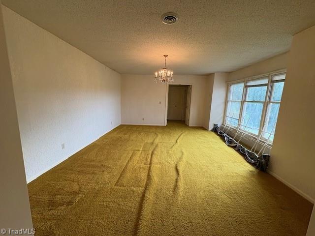 spare room featuring carpet floors, a chandelier, and a textured ceiling
