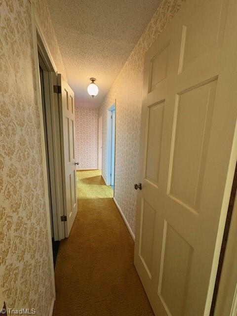 hallway with wallpapered walls, dark colored carpet, and a textured ceiling