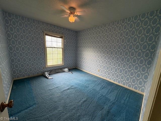 carpeted empty room featuring wallpapered walls, ceiling fan, and baseboards