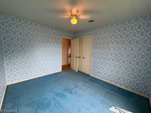 carpeted empty room featuring wallpapered walls and baseboards