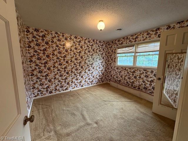 carpeted empty room featuring wallpapered walls and a textured ceiling