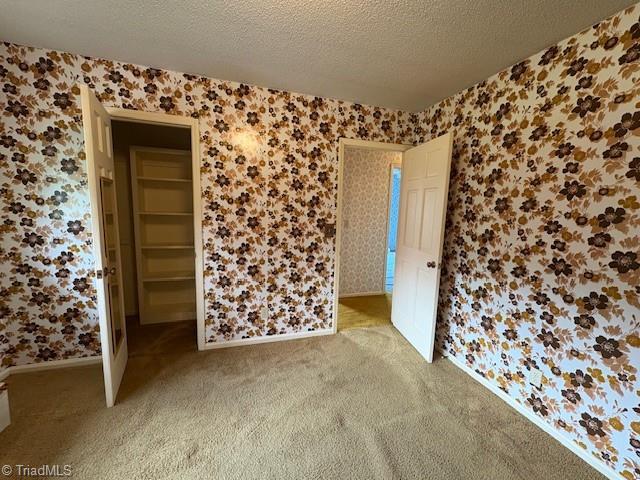 spare room with wallpapered walls, light colored carpet, a textured ceiling, and baseboards