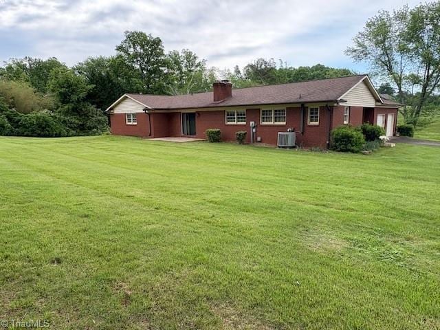 rear view of house with an attached garage, central AC unit, a lawn, a chimney, and asphalt driveway