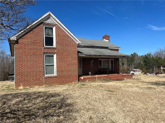 rear view of house with roof with shingles, a porch, a chimney, a lawn, and brick siding