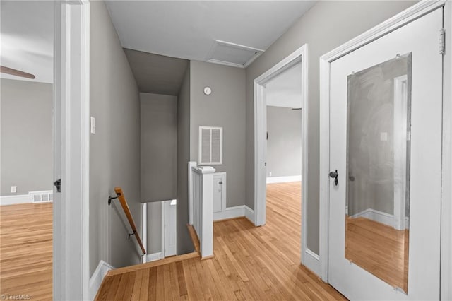 hallway with an upstairs landing, visible vents, attic access, and light wood-style floors