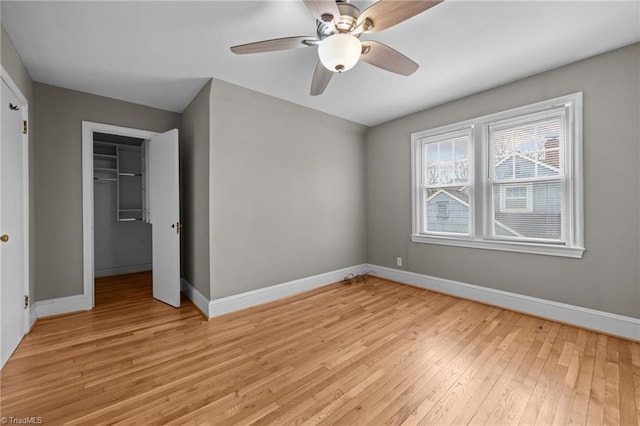 unfurnished bedroom featuring a closet, baseboards, a walk in closet, and light wood finished floors