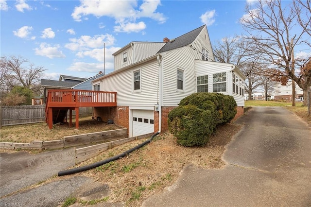 view of side of home featuring fence, driveway, a chimney, a garage, and a deck