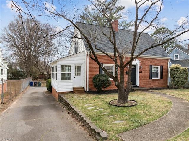 view of front facade featuring entry steps, fence, a shingled roof, brick siding, and a chimney