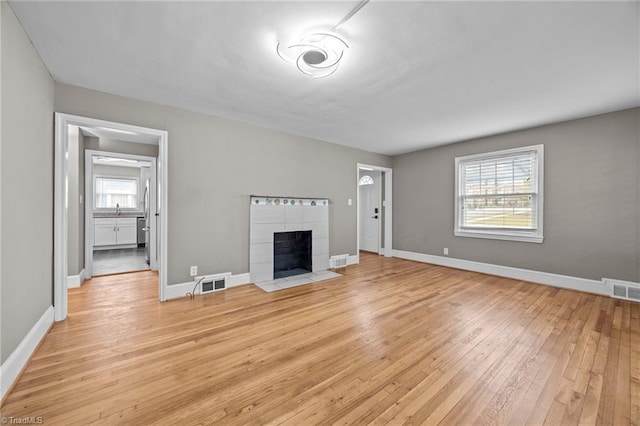 unfurnished living room featuring light wood finished floors, visible vents, a tiled fireplace, and baseboards