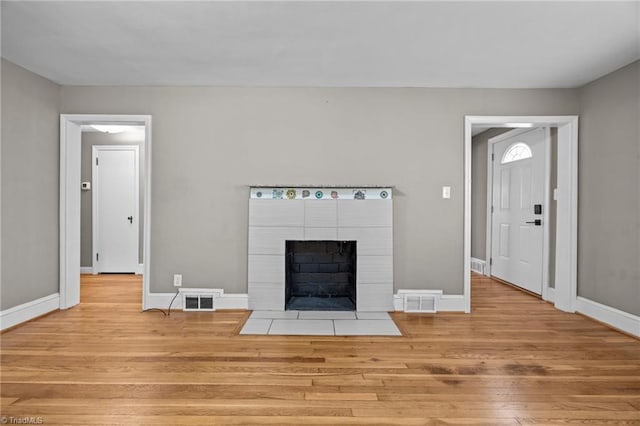 unfurnished living room with visible vents, wood finished floors, and a tile fireplace