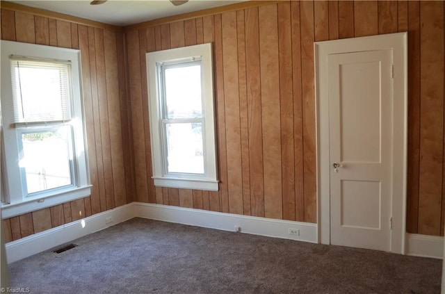 carpeted empty room with visible vents, a wealth of natural light, and wood walls