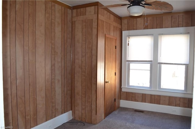 unfurnished room featuring a ceiling fan, wooden walls, carpet, and visible vents
