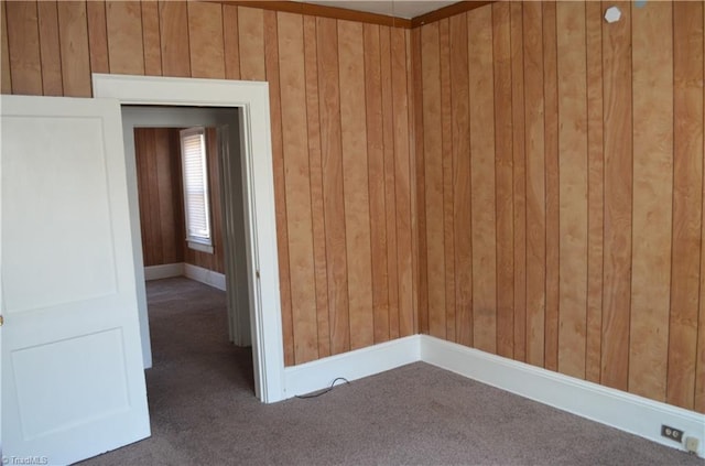 carpeted empty room featuring baseboards and wood walls