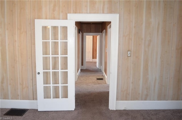 corridor with visible vents, carpet, and wooden walls