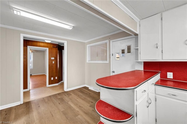 kitchen with ornamental molding, wood walls, white cabinetry, and light wood-type flooring