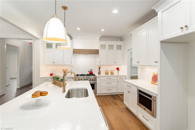 kitchen with premium range hood, white cabinets, sink, decorative light fixtures, and light hardwood / wood-style floors