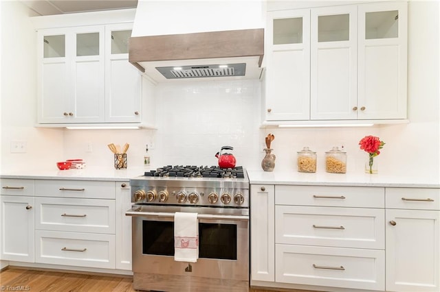 kitchen featuring premium range hood, white cabinets, light wood-type flooring, high end stove, and tasteful backsplash