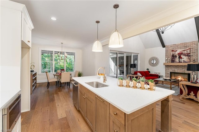 kitchen with a center island with sink, sink, hanging light fixtures, light hardwood / wood-style floors, and white cabinetry