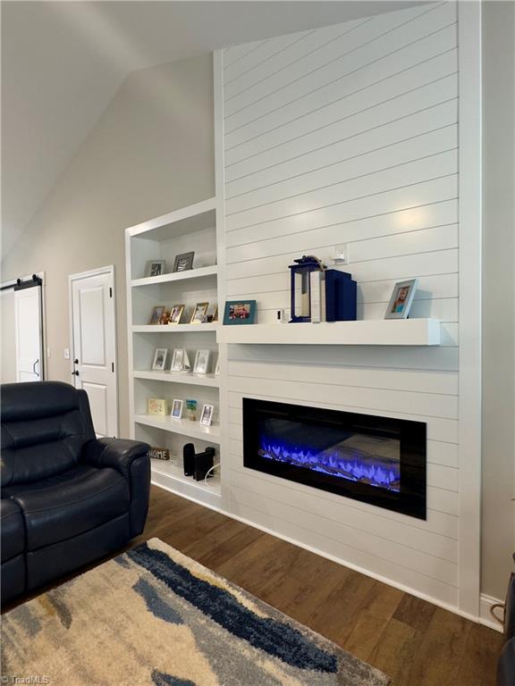 2968 Tobaccoville Rd, Tobaccoville, NC 27050 - living area featuring built in features, wood finished floors, vaulted ceiling, and a glass covered fireplace