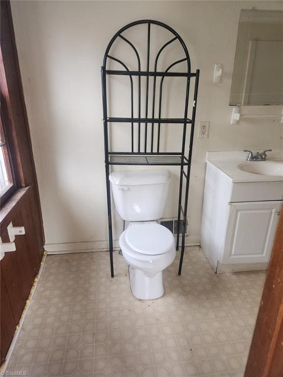 half bathroom with tile patterned floors, baseboards, toilet, and vanity