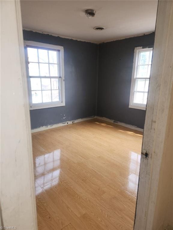 unfurnished room featuring visible vents, light wood-style flooring, and baseboards