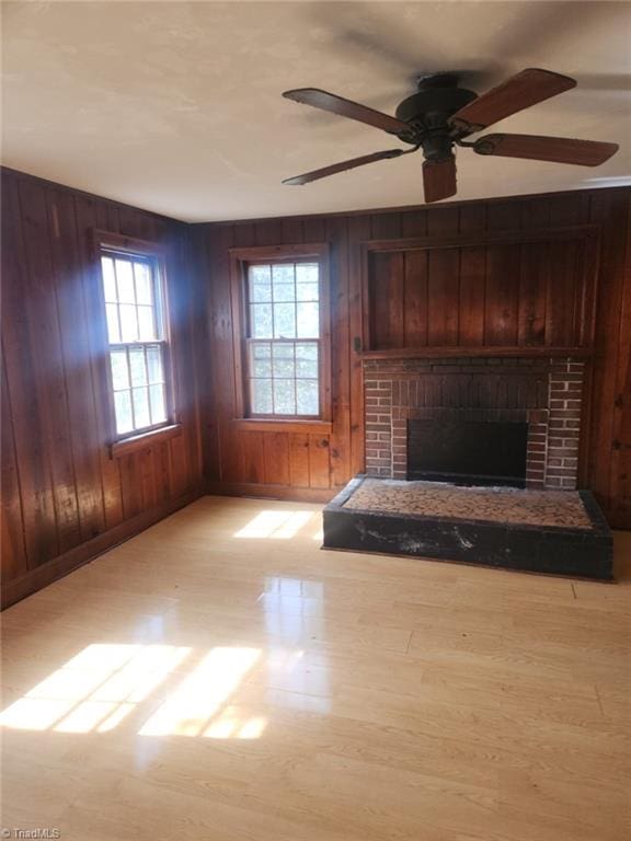 unfurnished living room with wood walls, a brick fireplace, and a ceiling fan