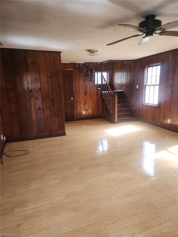 unfurnished room featuring light wood-type flooring, stairway, wooden walls, and ceiling fan