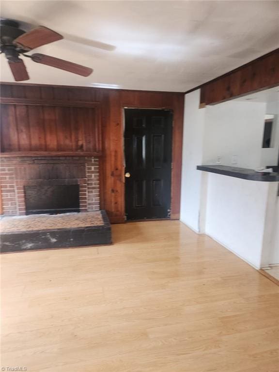 unfurnished living room with wood walls, a brick fireplace, and light wood-style flooring