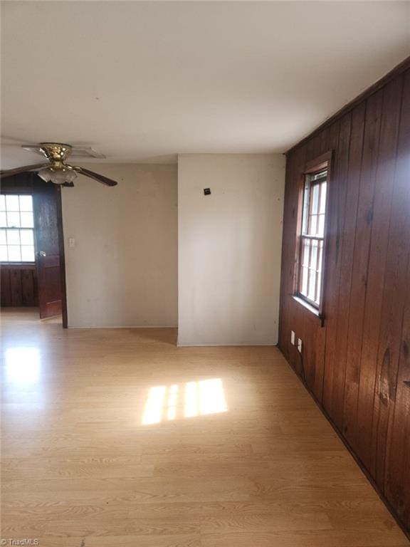 spare room featuring ceiling fan, light wood-style floors, and wood walls