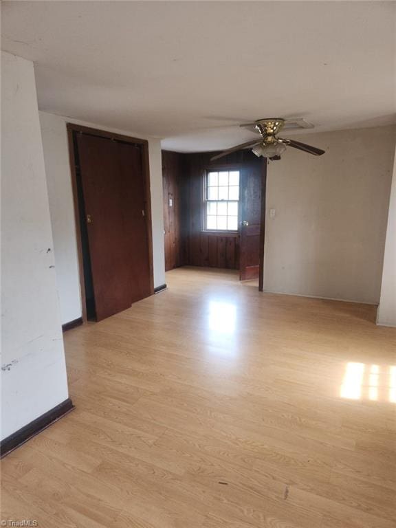 spare room with baseboards, light wood-style floors, and a ceiling fan