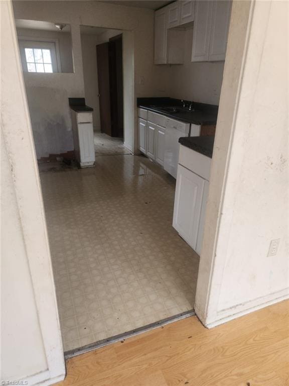 kitchen featuring a sink, dark countertops, light floors, and white dishwasher