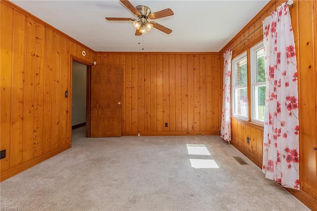 empty room featuring light carpet, wood walls, ceiling fan, and ornamental molding