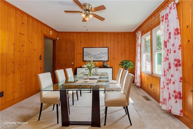 dining room with light carpet, wood walls, ornamental molding, and ceiling fan