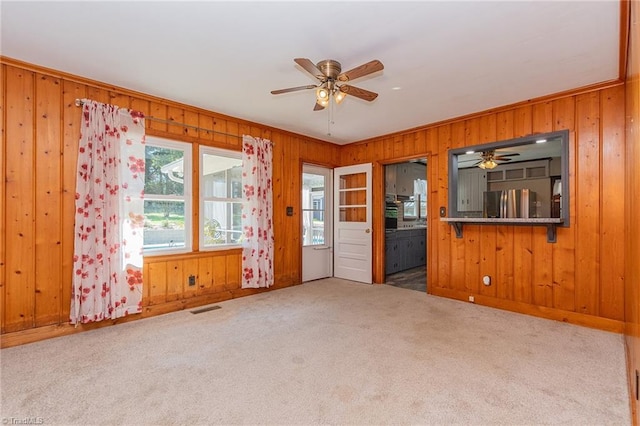 unfurnished living room featuring crown molding, carpet floors, wooden walls, and ceiling fan