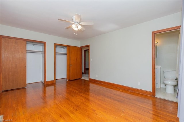 unfurnished bedroom featuring connected bathroom, two closets, hardwood / wood-style flooring, and ceiling fan