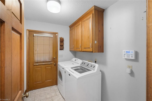 clothes washing area featuring light tile patterned floors, washer and clothes dryer, cabinets, and a textured ceiling