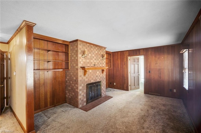 unfurnished living room featuring wood walls, ornamental molding, a brick fireplace, and light colored carpet