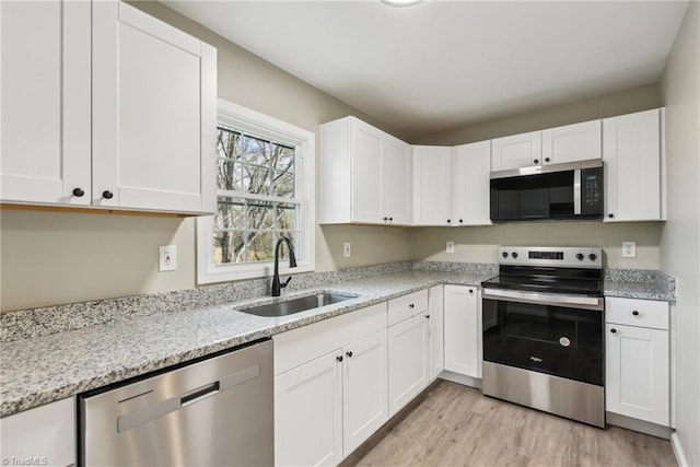 kitchen with stainless steel appliances, white cabinetry, sink, and light stone counters