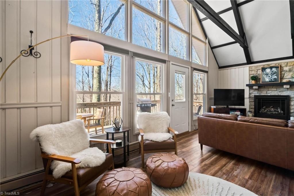 721 Pine Ridge Rd, Beech Mountain, NC 28604 - living area featuring dark wood-style flooring, a stone fireplace, beamed ceiling, high vaulted ceiling, and a baseboard radiator