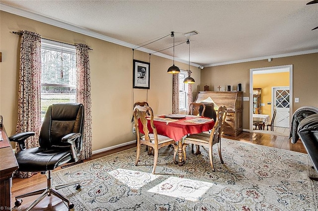 dining space with baseboards, a textured ceiling, ornamental molding, and wood finished floors