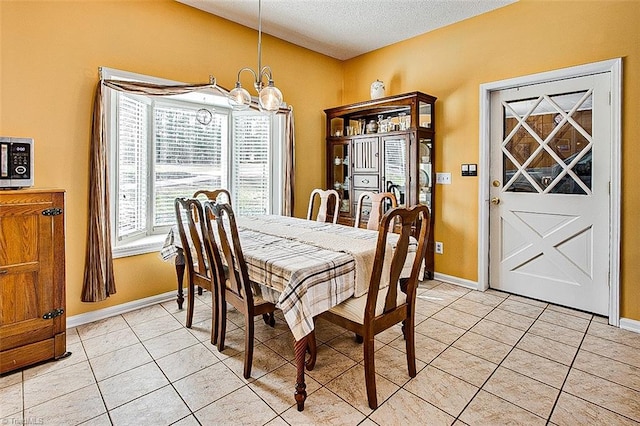 dining area with light tile patterned floors, a textured ceiling, baseboards, and a notable chandelier